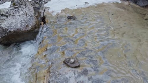 Nahaufnahme von Wasser, das während des Tauwetters im frühen Frühling über bunt strukturierte Felsen fließt.