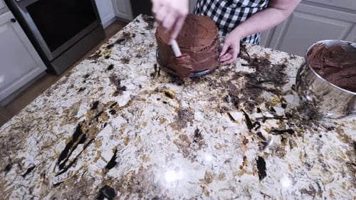 Woman Decorates Chocolate Cake with Frosting in Kitchen
