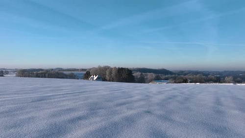 A serene winter scene featuring a snowcovered field and distant buildings under a clear blue sky.