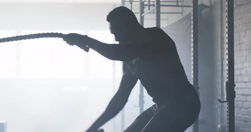 Exercising with battle ropes, man training in gym for strength and endurance