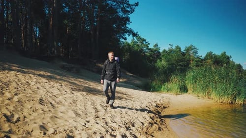Man Hiking Along Lake Shore on Sunny Day