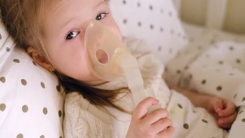 Bébé est allongé dans son lit sous une couverture et respire dans un masque nébuliseur à inhalation