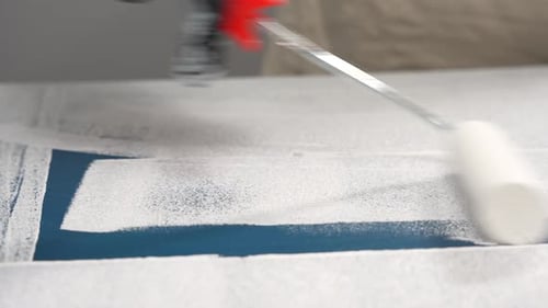 Paint Roller Applying White Paint to Blue Surface