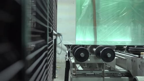 Transport großer Objekte in einer Fabrik von Maschine zu Maschine. Eine große Glasscheibe auf einer Transportrolle