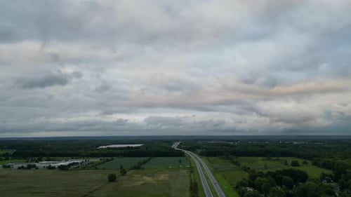 A broad aerial view showcasing a rural highway stretching through vast fields under an overcast sky.