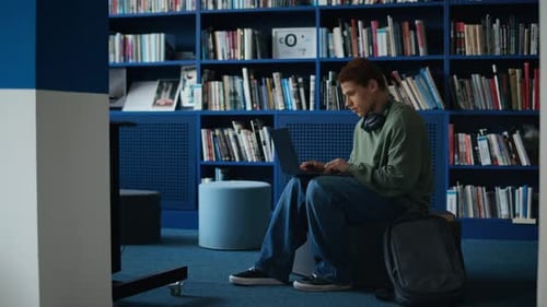 Estudiante birracial trabajando en una computadora portátil en la biblioteca universitaria moderna