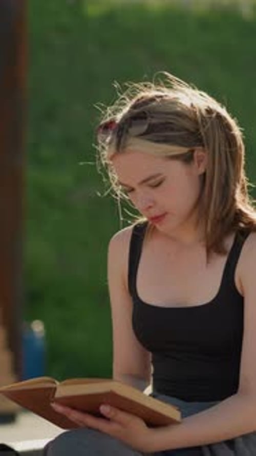 Woman Sits Outside, Reading Book on Sunny Day