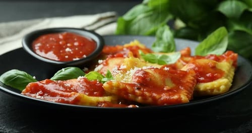 Adding parmesan cheese onto delicious ravioli with tomato sauce and basil at table, closeup
