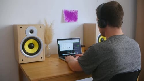 A Man in a Home Music Studio Sits at a Desk with Equipment and Looks at a Computer