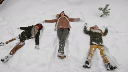Happy Caucasian Mom and Children Making Snow Angels during Winter Walk