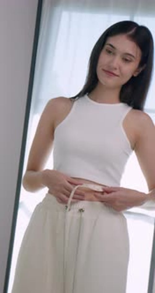Young Woman Measuring Waist at Home in Mirror