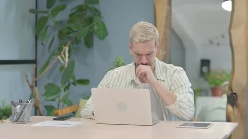 Man Coughing While Working on Laptop at Home