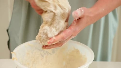 Close-up of hands kneading sticky bread dough in a white bowl, capturing the tactile process of home
