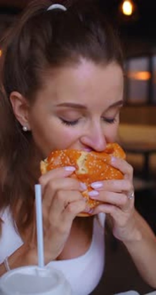 Closeup Footage of a Young Woman Eating Hamburger at a Cafe