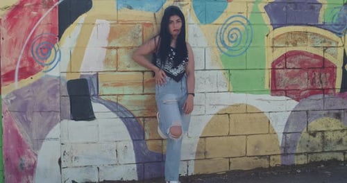 In Straßenmode gekleidet steht ein Mädchen in der Stadt mit einer mit Graffiti bedeckten Wand im Hintergrund.