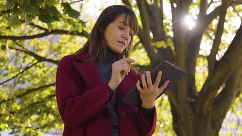 An Attractive Middleaged Caucasian Woman Works on a Tablet in a Park Closeup From Below