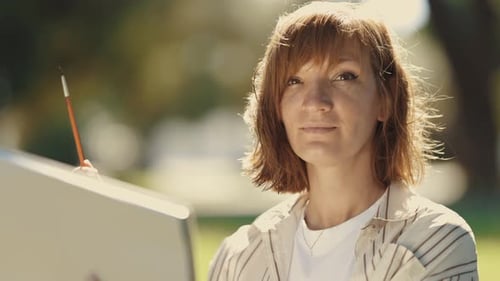Adult Woman Artist Sitting in the Park Holding a Sketchbook