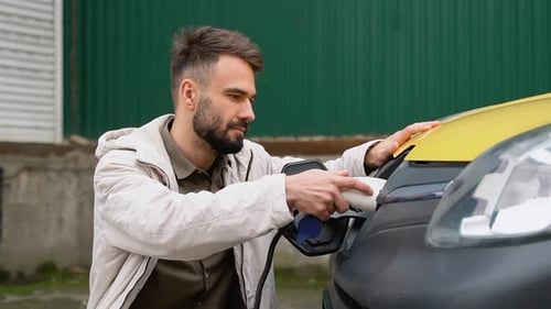 Stylish Spanish Man Plugging in Charging Cable to Electric Vehicle and Charges Batteries