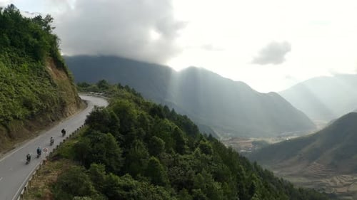A small group of motorcycle riders on a winding rural mountain road in the Sapa mountain range, aeri