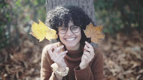 Fille timide et stupide aux boucles afro jouant avec les feuilles sèches d'automne