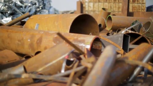 Panning shot of rusty metal pipes and scrap in a junkyard during daytime