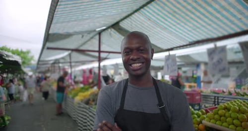 Afroamerikanischer Straßenverkäufer steht mit verschränkten Armen an einem Verkaufsstand mit Produkten im Freien und drückt