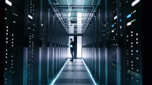 Un
ingeniero de TI masculino trabaja en una computadora portátil en un centro de Big Data. Se ven filas de servidores en rack.