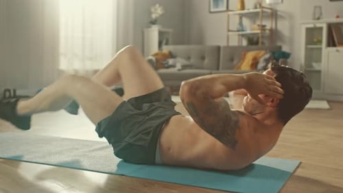 Der starke athletische, hemdlose, fitte Mann in grauen Shorts macht zu Hause in seiner Kleidung Crisscross-Crunch-Übungen