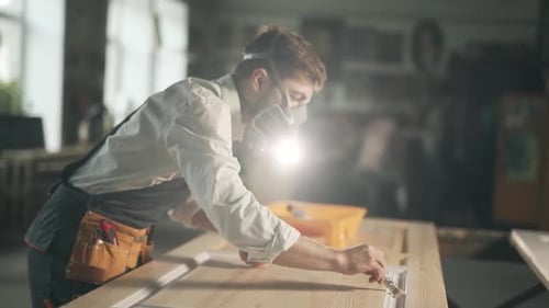 close-up side view of a man in work uniform and respirators paints a wooden product with a roller in