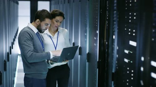 Male IT Specialist Holds Laptop and Discusses Work with Female Server Technician. They're Standing