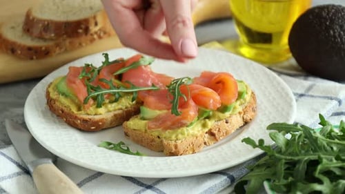 Preparing gourmet avocado salmon toast with arugula garnish