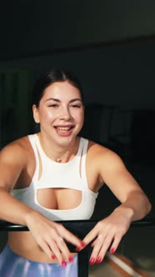 Joven y enérgica chica de fitness con top blanco y leggings azules iridiscentes haciendo ejercicios saltando sobre mo