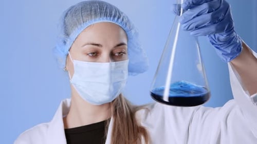Woman Scientist Examines Flask with Blue Liquid