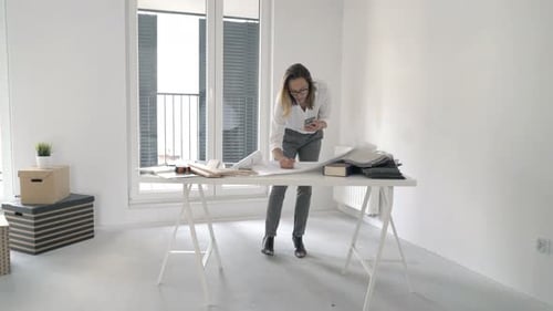 Woman Using Phone With Blueprints in Apartment