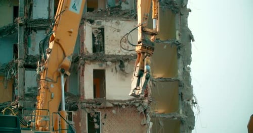 Long boom excavator drilling and demolishing the high rise building, concrete blocks falling down th