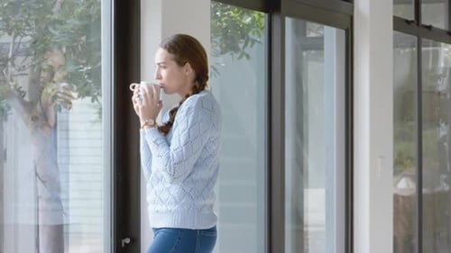 Thoughful caucasian woman with cup of coffee in sunny living room, slow motion