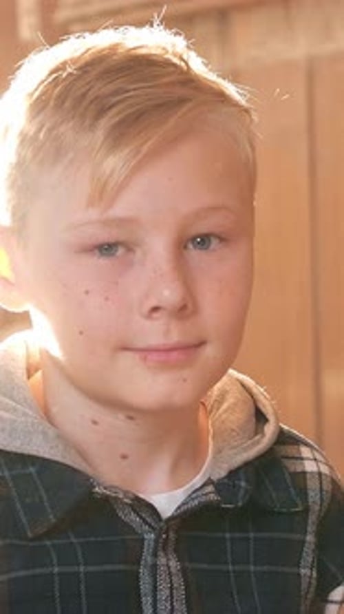 Jeune garçon aux cheveux blonds clairs et aux taches de rousseurs sourit chaleureusement dans une pièce ensoleillée présentant un