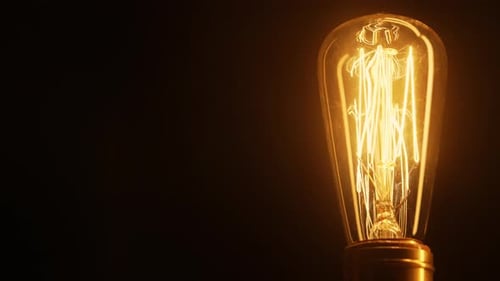 Vintage Lightbulb Filament Glowing Against Black Background
