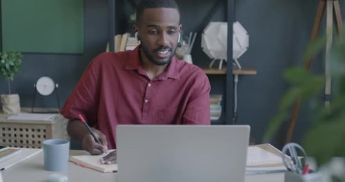 Afroamerikanischer Geschäftsmann, der Online-Videoanruf mit Laptop und drahtlosen Kopfhörern tätigt