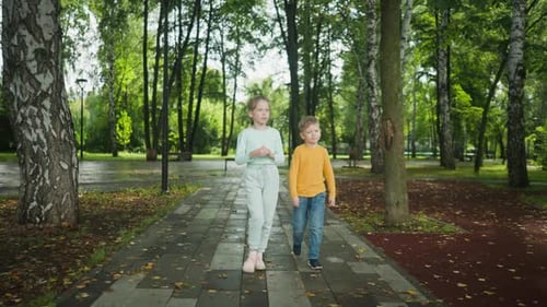 Kids Walking on TreeLined Path in Park After Rain