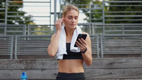 Woman Puts in Earphones and Uses Phone Outdoors