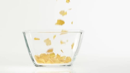 Fresh healthy food. Yellow cornflakes fall in a transparent square bowl on a white background