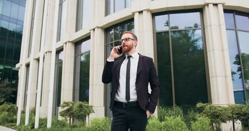 Joven empresario exitoso de pie cerca del edificio de oficinas después de un día de trabajo usando un teléfono móvil