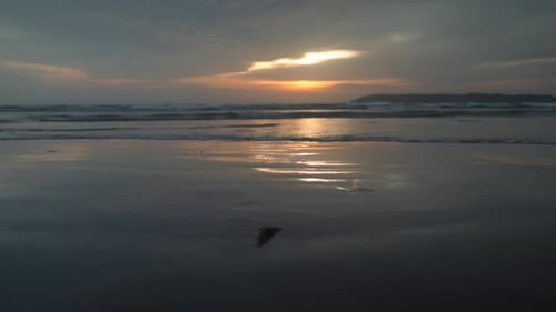 Seascape view of ocean waves crashing on the sandy coastline, at sunset, on a cloudy evening