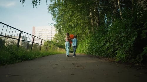 Back View of Kids Walking Along Leafy Path with Fence and Building Behind