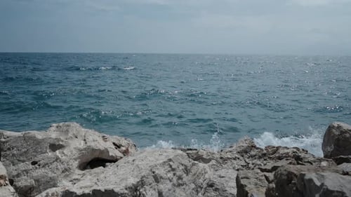 The sea waves crash against large rocks, clear weather, slow motion.