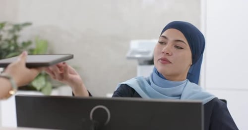O visitante está estendendo o tablet enquanto a recepcionista está se inclinando para revisar a fatura para confirmar na recepção