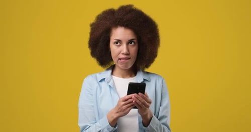 Young Happy Smiling African American Woman Typing a Text Message on a Cellphone Isolated on Orange