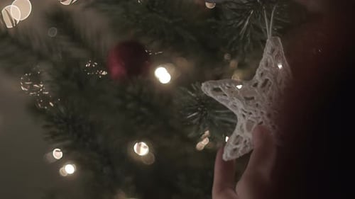 Hands Decorating Lit Christmas Tree With Ornaments