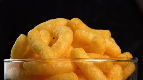 Corn cheese chips rotate in a glass bowl closeup. Crispy cheese snack. Crispy fluffy corn sticks